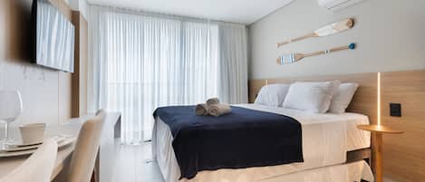 Una habitación de hotel moderna con cama, televisión, zona de comedor y vistas al exterior.