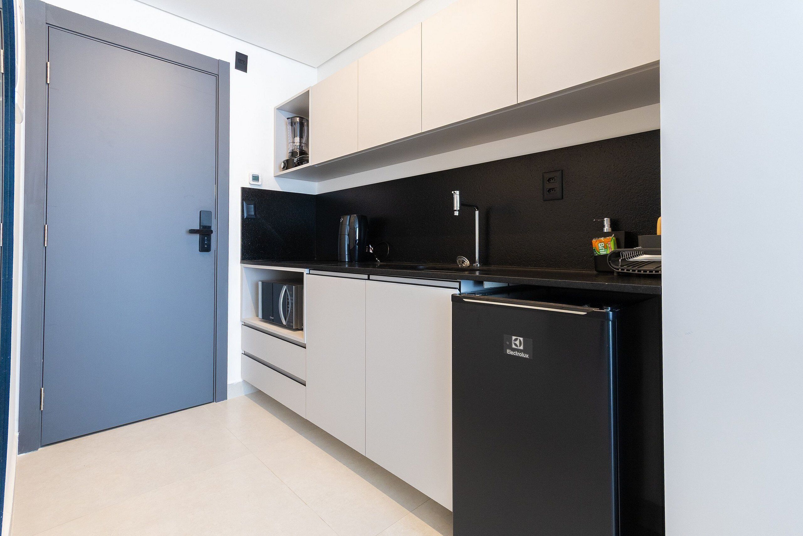 Una cocina moderna con un refrigerador negro, armarios blancos y una cafetera.