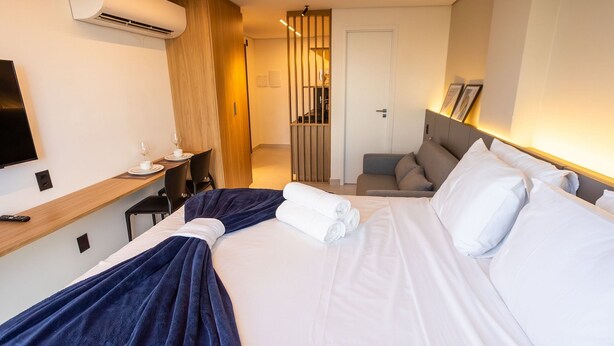 A hotel room with a bed, a desk with a chair, a TV, and a wall-mounted air conditioner. - Azimut With Direct Beach Access and Sea View by Carpediem (Cabedelo)