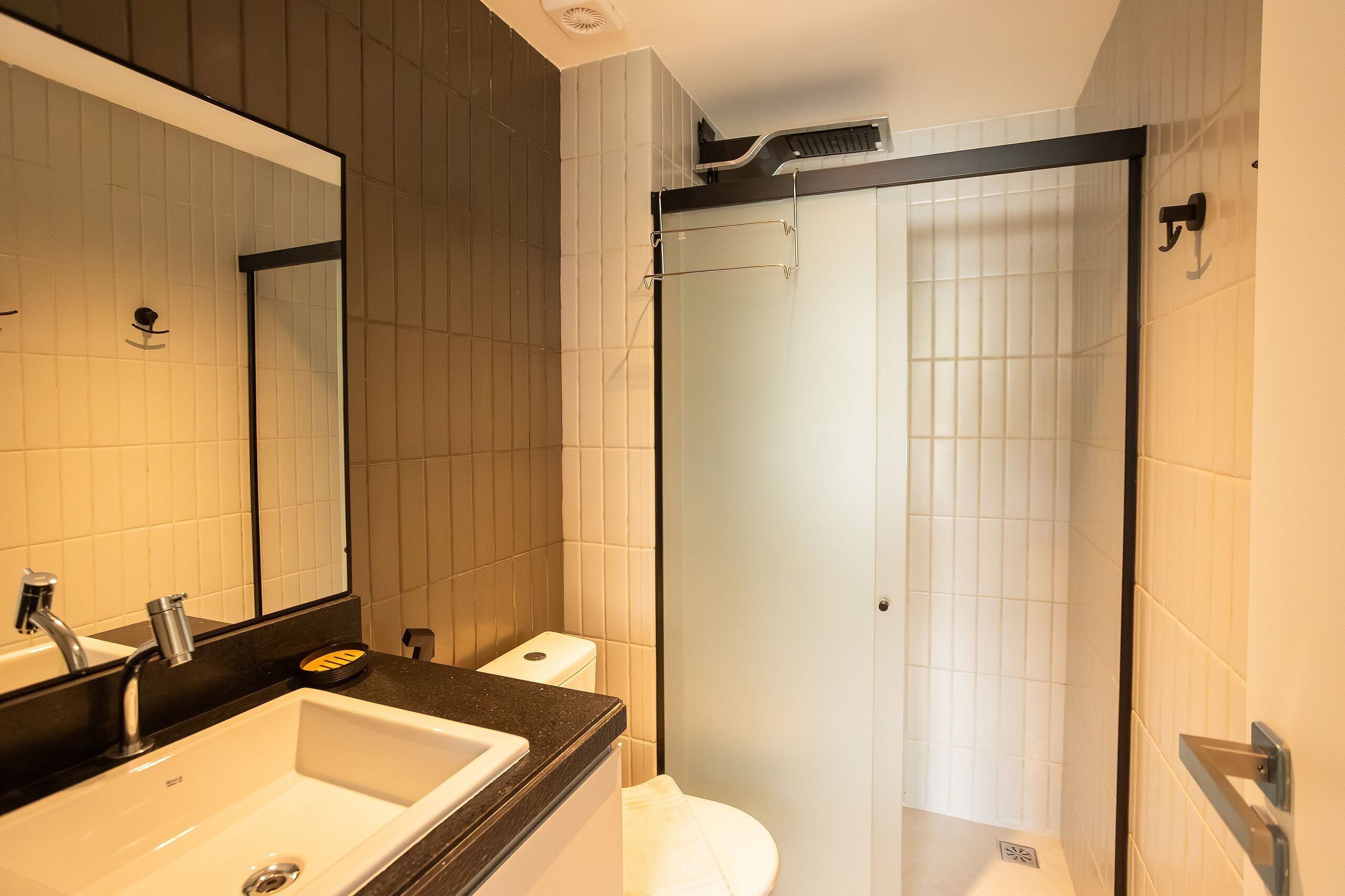 Baño con lavamanos, espejo, inodoro y cabina de ducha con paredes de vidrio.