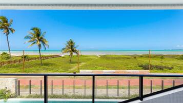 Varanda com vista para uma praia, palmeiras e um céu azul límpido.