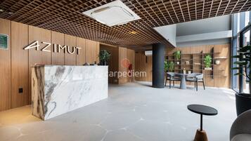 A reception area with a marble counter, wooden paneling, a grid ceiling, and a seating area with a table and chairs.