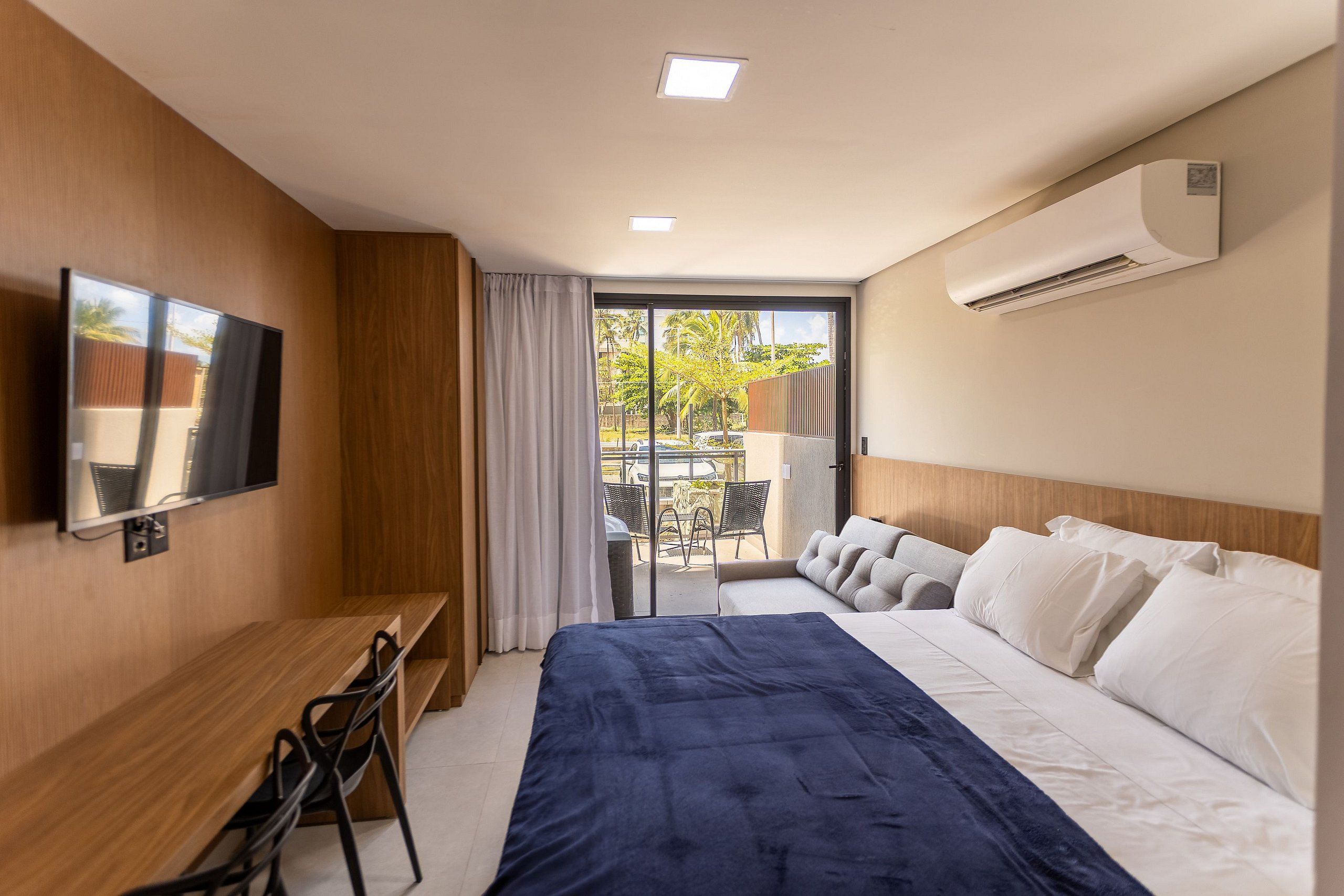 Quarto de hotel com cama, escrivaninha, televisão e varanda com vista para o exterior.