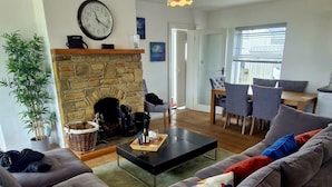 Een woonkamer met een open haard, een eethoek en een bank met kleurrijke kussens.