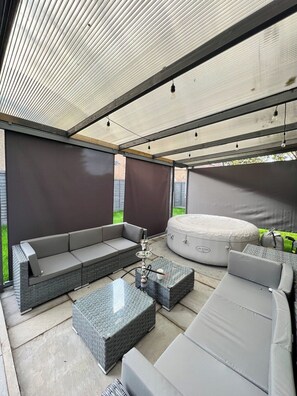 Un espace extĂ©rieur amĂ©nagĂ© avec un salon de jardin, comprenant un canapĂ©, un pouf et une table, ainsi quâun jacuzzi.