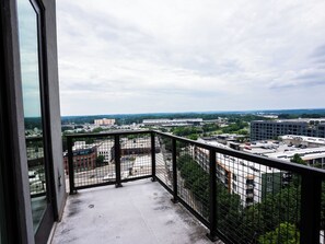 A balcony with a metal railing overlooking a cityscape with buildings and greenery.