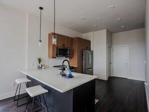 A modern kitchen with a central island, stainless steel appliances, wooden cabinets, and pendant lighting.