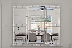Ein Essbereich mit Tisch und Stühlen, ein Fenster mit Blick auf einen Garten und ein Deckenventilator.
