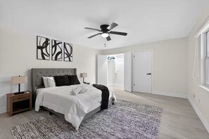 Ein Schlafzimmer mit Bett, Nachttischen, Deckenventilator, abstrakten Wandbildern und einem gemusterten Teppich.