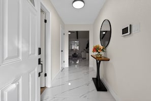 A hallway with white doors, a marble floor, a round mirror, and a small table with flowers. - Private Pool-Paradise - 5BR- Close to Everything (Houston)