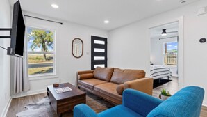 A modern living room with a sofa, a coffee table, a TV, and a view of the outdoors.