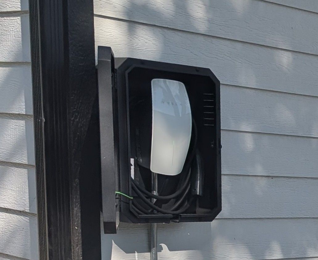 A black electrical box mounted on a wall with horizontal siding.