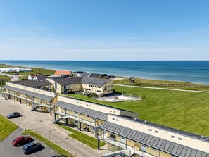 A coastal hotel with a parking area, a covered walkway, and a view of the sea.