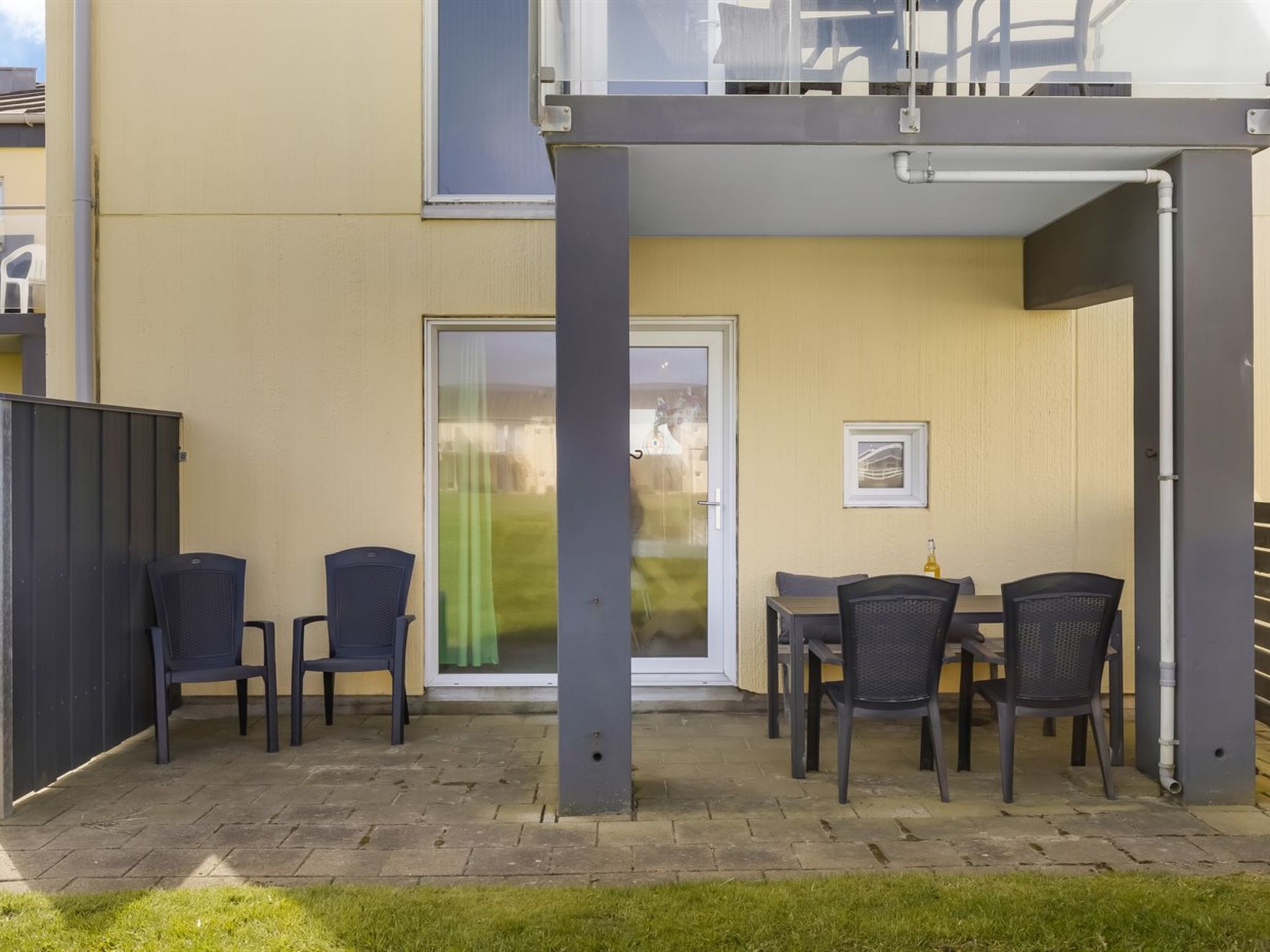 Un espace patio avec une table et des chaises, une porte-fenêtre coulissante et un petit tableau encadré accroché au mur.