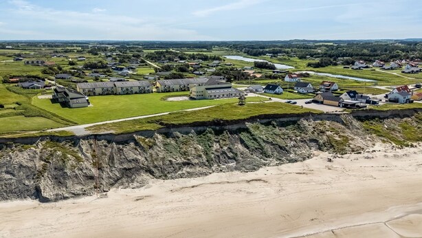 Vista aérea de una zona costera con edificios residenciales, una playa y un acantilado rocoso.