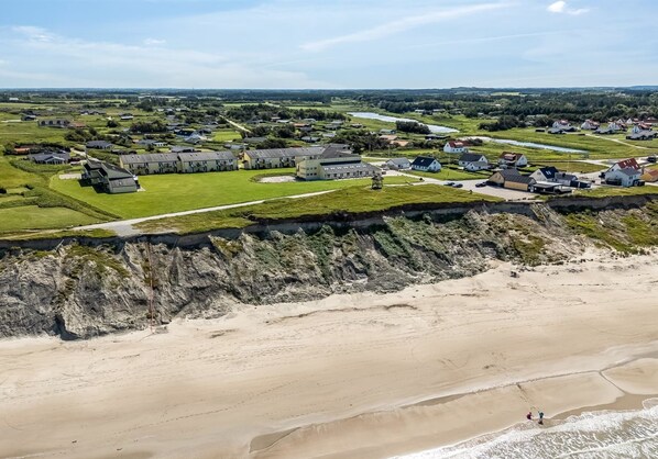 An aerial view of a coastal area with residential buildings, a beach, and a cliff.