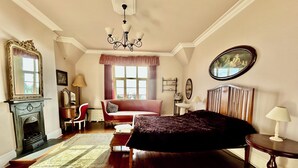 A bedroom with a fireplace, a bed, a sofa, a chair, a round table, and a chandelier. - Victorian Deco House - 5-bedroom house in Ventnor perfect for family getaways (Ventnor)