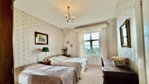 A room with two beds, a chandelier, a window with a view, and a mirror on the wall. - Victorian Deco House - 5-bedroom house in Ventnor perfect for family getaways (Ventnor)