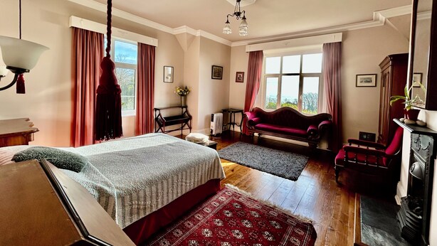 A room with a bed, a red sofa, a piano, and a fireplace. - Victorian Deco House - 5-bedroom house in Ventnor perfect for family getaways (Ventnor)