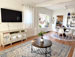 A living room with a TV, a wooden cabinet, a round coffee table, and a dining area with chairs and a table.