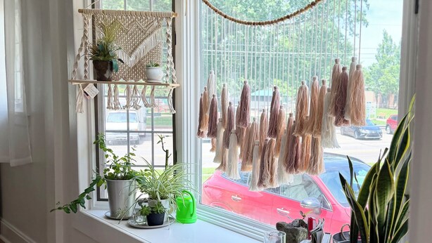 Una habitación con un ventanal grande, un tapiz de macramé y varias plantas en macetas.