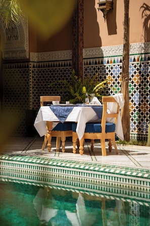 Una mesa de comedor con sillas, una piscina y un muro estampado al fondo.