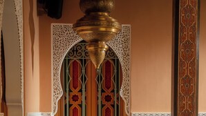 Ein Zimmer mit Wand aus gemusterten Fliesen, einem dekorativen Fenster und zwei rot gepolsterten Sesseln.