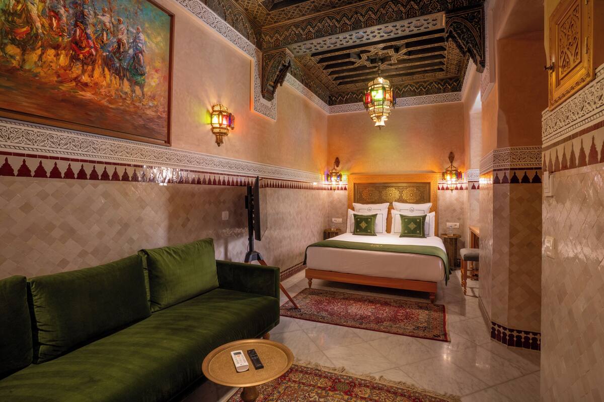 A room with a bed, a green sofa, a small round table, and a painting on the wall.