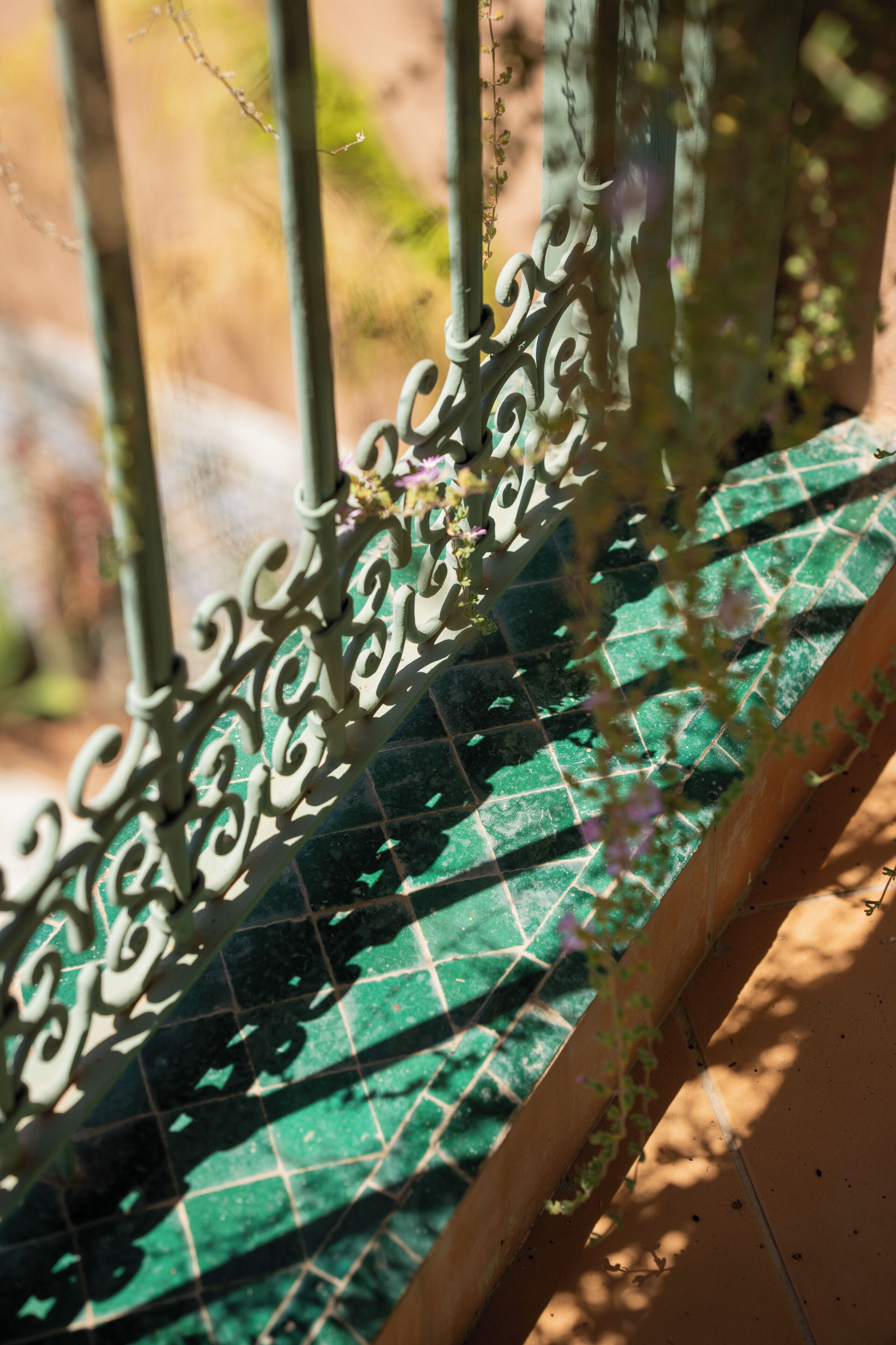 A balcony with a green tiled floor and ornate metal railings.