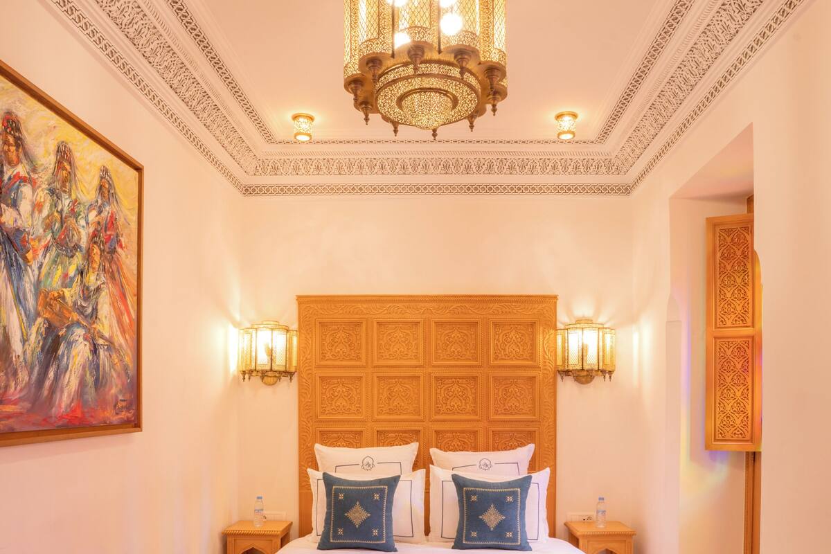 A room with a large bed, ornate ceiling, and a chandelier.