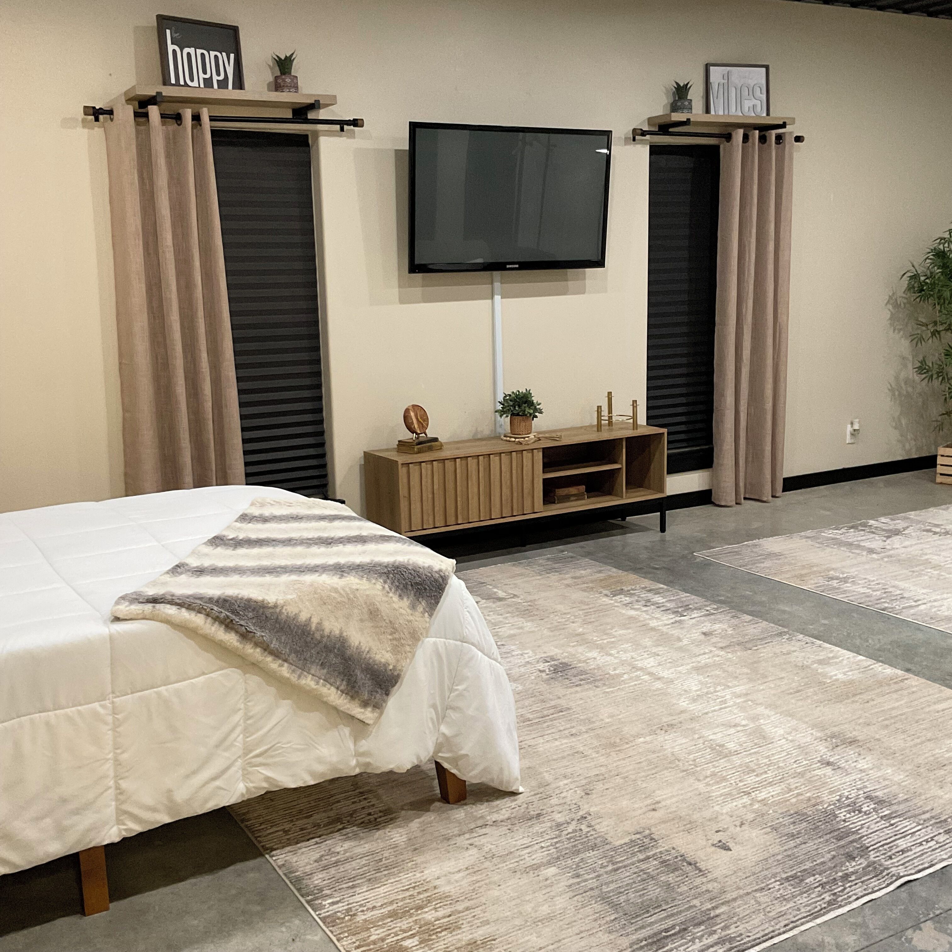 Un dormitorio con una cama, un televisor montado en la pared y un pequeño aparador de madera debajo.