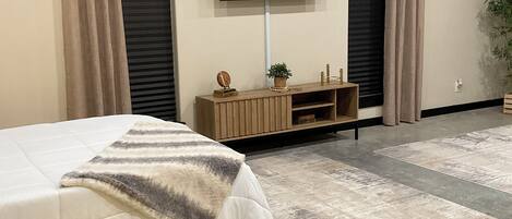 Un dormitorio con una cama, un televisor montado en la pared y un pequeño aparador de madera debajo.