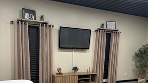 A bedroom with a bed, a TV mounted on the wall, a wooden console table, and a potted plant. - The serenity studio near route 66 (Webb City)