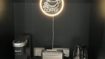 Una macchina da caffè, un tostapane e una caffettiera su un tavolo, con un neon a forma di tazza di caffè sopra.