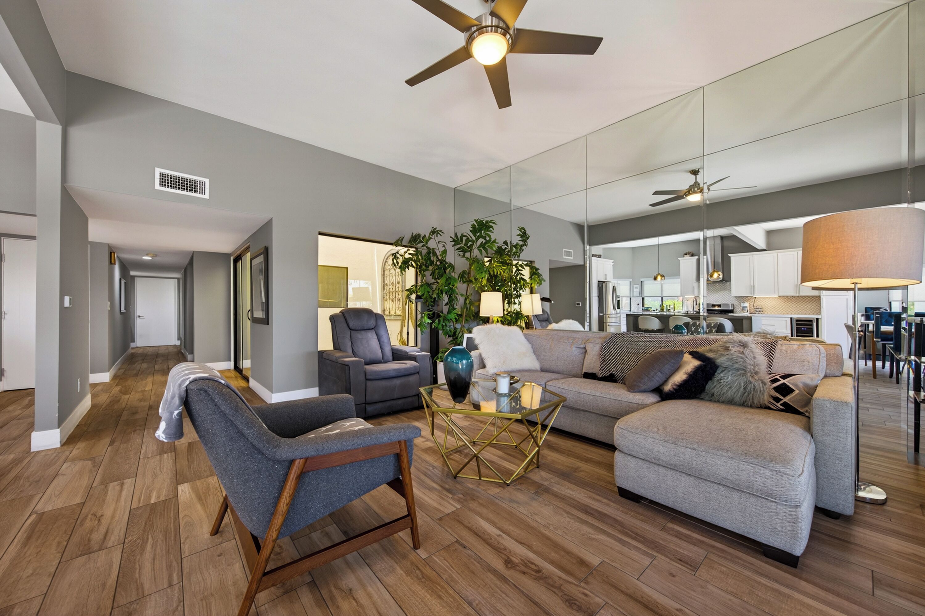 A modern living room with a sofa, armchair, coffee table, and ceiling fan.