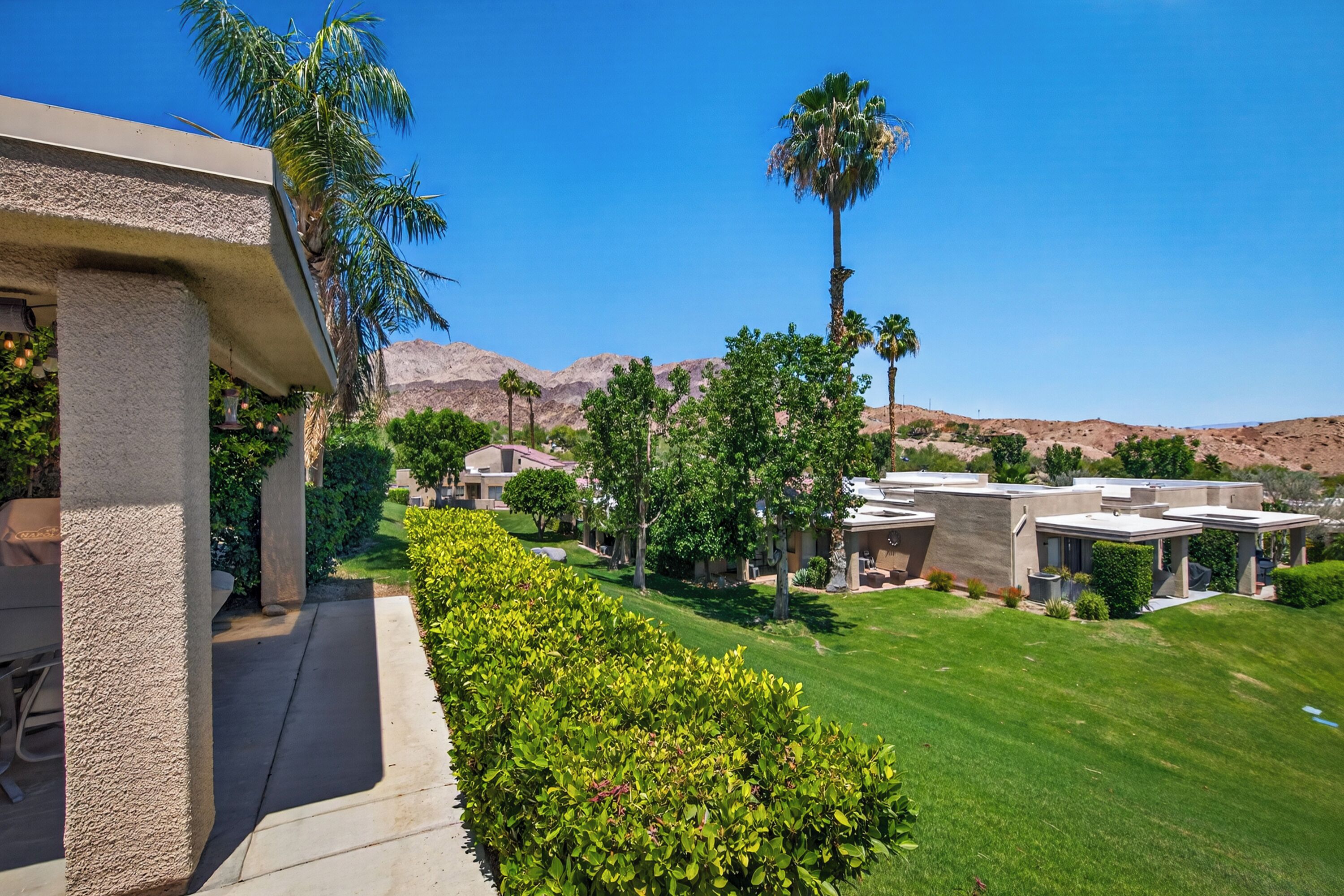 A residential area with modern houses, a well-maintained lawn, and palm trees.