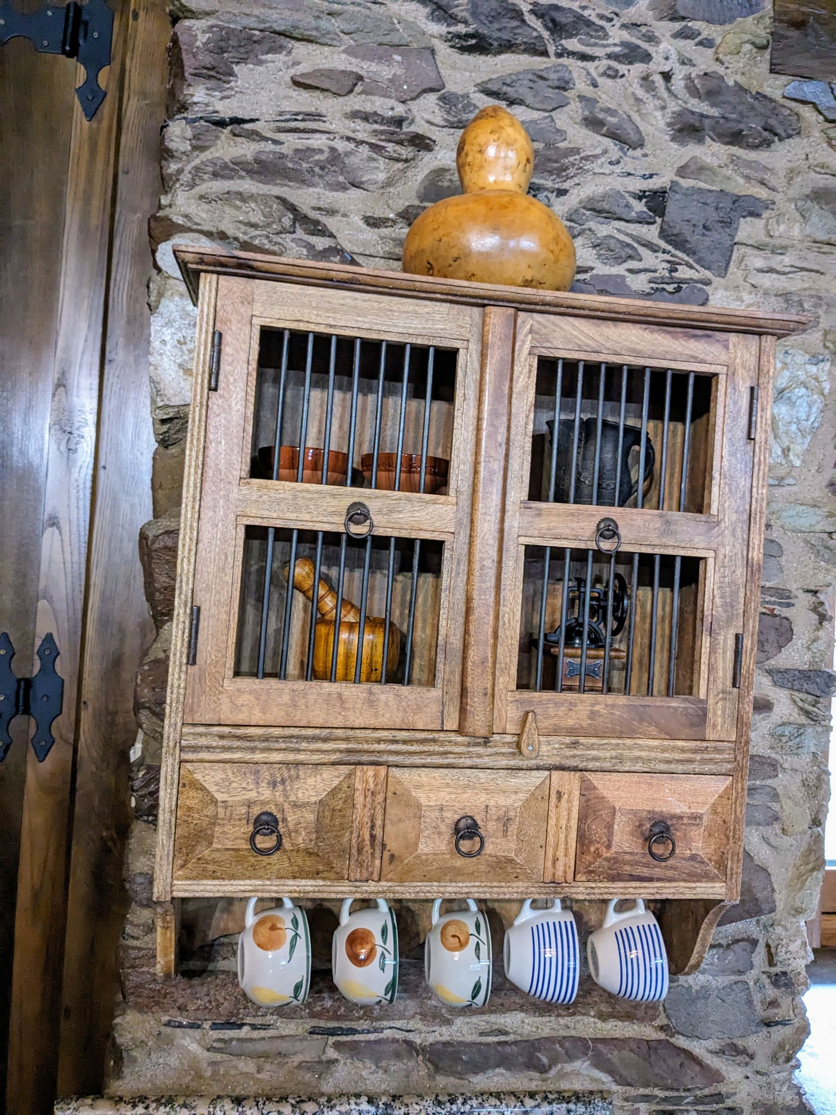 A wooden cabinet with glass doors, containing various kitchen utensils and decorative items.