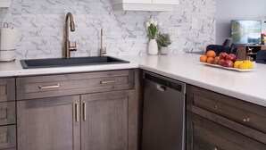 Eine moderne Küche mit weißen Schränken, einer Marmor-Spritzschutzwand, einem eingebauten Geschirrspüler und einer Obstschale auf der Arbeitsplatte.