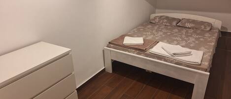 A bedroom with a bed, a bedside table, a dresser, and a small table with towels.