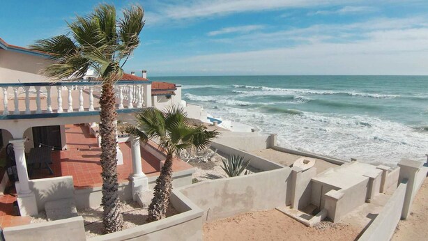 A coastal property with a balcony overlooking the sea, palm trees, and a white building with red tiles. - Beachfront Home in Rocky Point Casa Alhaja (Puerto Peñasco)