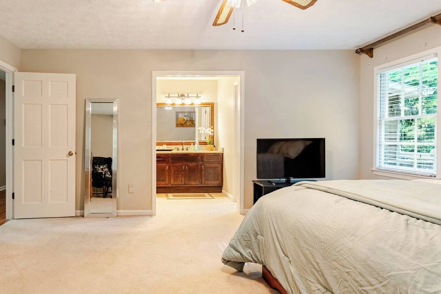 A bedroom with a bed, a TV, a bathroom with a mirror and sink, and a door leading to another room.