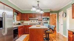 Una cocina con armarios de madera, un refrigerador de acero inoxidable, un microondas y una isla grande con taburetes de bar.