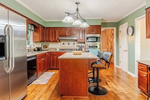 A kitchen with wooden cabinets, a stainless steel refrigerator, a microwave, and a large island with bar stools.