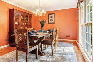 A dining room with a wooden table, chairs, a chandelier, and a window.