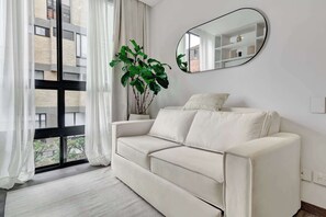 A modern living room with a white sofa, a large mirror, and a potted plant. - w* | Luxury & Cozy Loft in Chapinero (Bogotá)