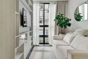 A modern living room with a sofa, a television on a shelf, a large window with curtains, and a potted plant. - w* | Luxury Loft in Chapinero w/ Gym (Bogotá)