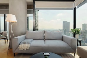 A modern living room with a grey sofa, a floor lamp, a remote control on a coffee table, and a city view through large windows. - w* | Spacious 1BR in Juarez (Ciudad de México)