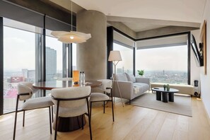 A modern living room with a dining table, chairs, a sofa, and a floor lamp. Large windows offer a city view. - w* | Spacious 1BR in Juarez (Ciudad de México)
