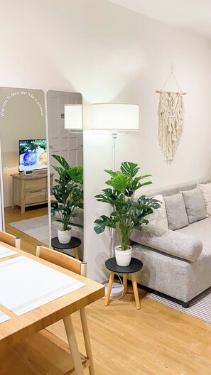 Uma sala de estar com sofá, mesa de centro, abajur, televisão e duas plantas em vasos.
