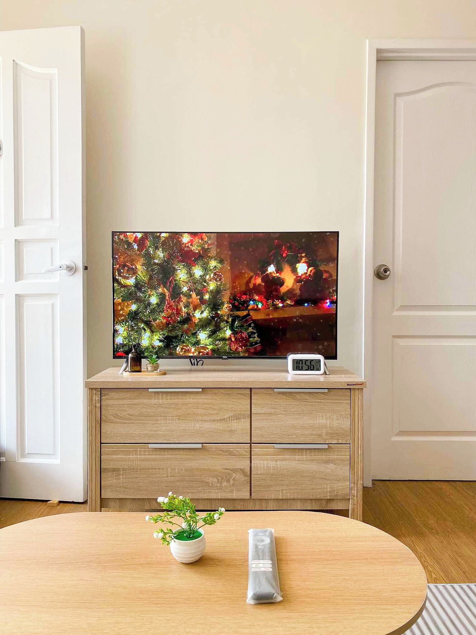 A television on a wooden cabinet, a clock, and a small table with a potted plant.